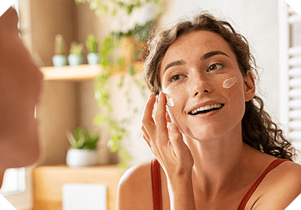 An image of a woman applying cream to her face in the bathroom
